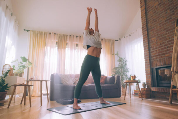 A woman practicing yoga in her living room, surrounded by natural light and a serene atmosphere. - Fitsse