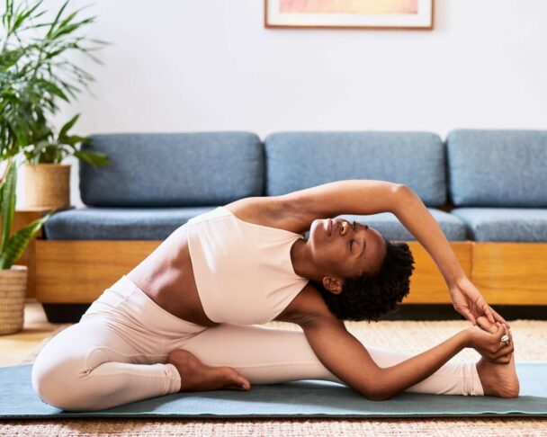 A woman practicing yoga in her living room, surrounded by natural light and a serene atmosphere. - Fitsse