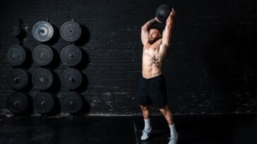 A man lifts a kettlebell overhead, showcasing strength and determination in his workout routine. - Fitsse