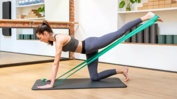 A woman performs a yoga pose using a green resistance band, showcasing strength and flexibility in her workout routine. - Fitsse