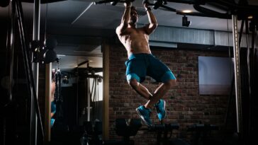 A man performs a pull-up on a bar in a gym, showcasing strength and determination in his workout routine. - Fitsse