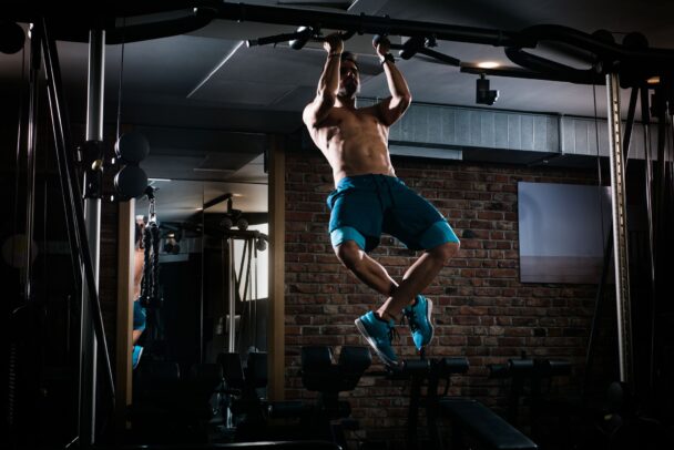 A man performs a pull-up on a bar in a gym, showcasing strength and determination in his workout routine. - Fitsse