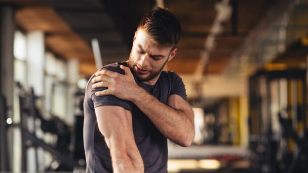 A man clutches his arm in a gym, showcasing his commitment to training and physical fitness. - Fitsse