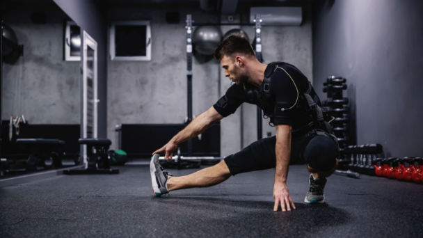 A man performing a stretch in a gym, focusing on flexibility and strength training. - Fitsse