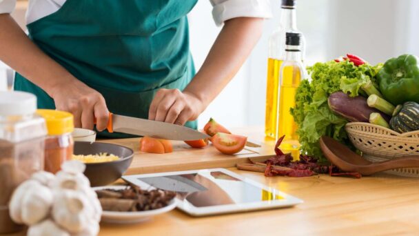 A woman skillfully chops fresh vegetables on a wooden table, preparing for a healthy meal. - Fitsse