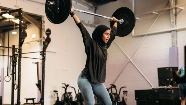 A woman in a hijab confidently lifts a barbell in a gym, showcasing strength and determination. - Fitsse