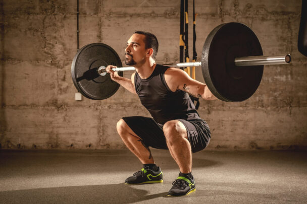 A man performs a squat with a barbell in a gym, showcasing strength and proper form during his workout. - Fitsse